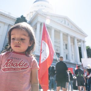 Child in front of flag and building.